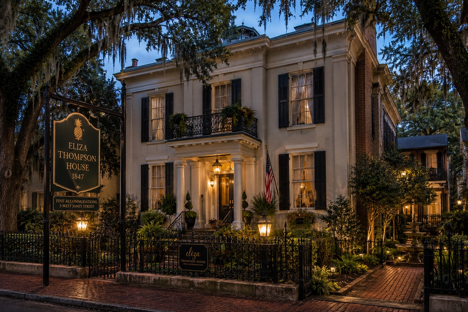 The Eliza Thompson House bed and breakfast in Savannah lit up at dusk, with its columned entrance, iron fence, and garden visible from Jones Street.