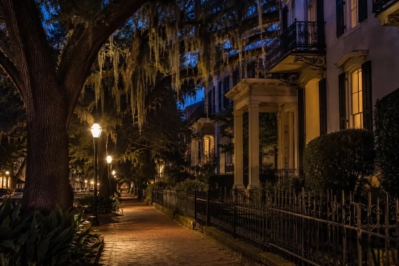 Historic Savannah street at night beneath live oaks and warm street lamps.